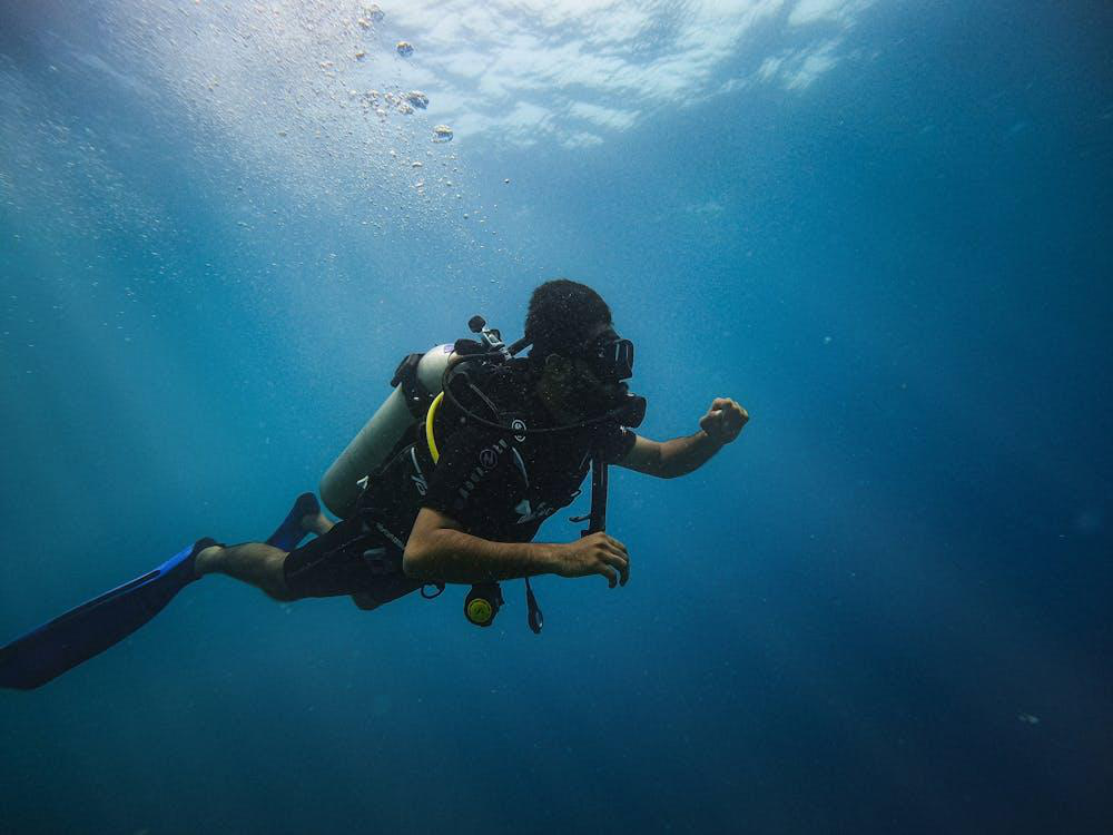 A man in a black wetsuit scuba diving underwater, exploring the depths of the ocean.